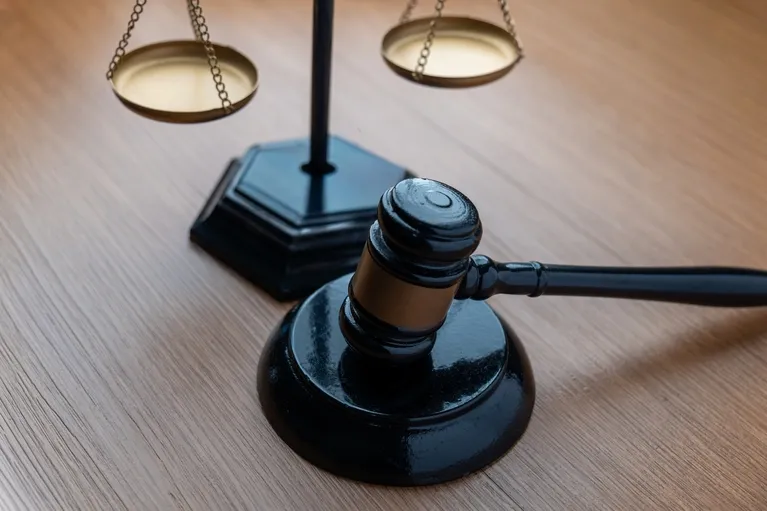 Black wooden judge’s gavel and brass balance scales on a light wooden surface.