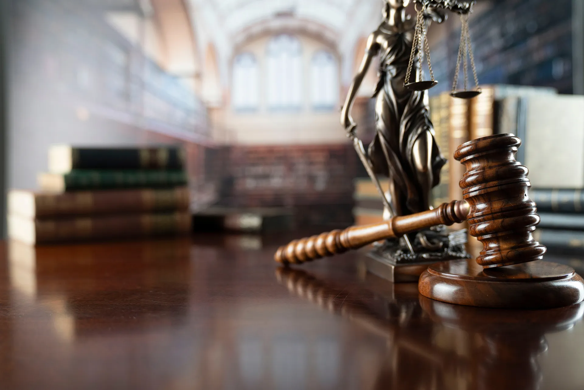 Close-up of a wooden judge's gavel, Lady Justice statue, and stacked legal books in a courtroom.