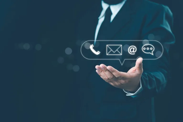 Businessman in dark suit presenting floating contact icons including phone, email, at symbol, and chat bubble.