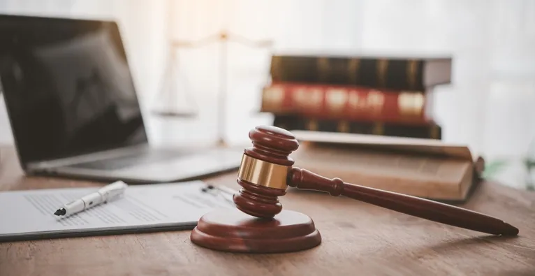 Wooden judge's gavel on desk with legal books, laptop, and documents in background.