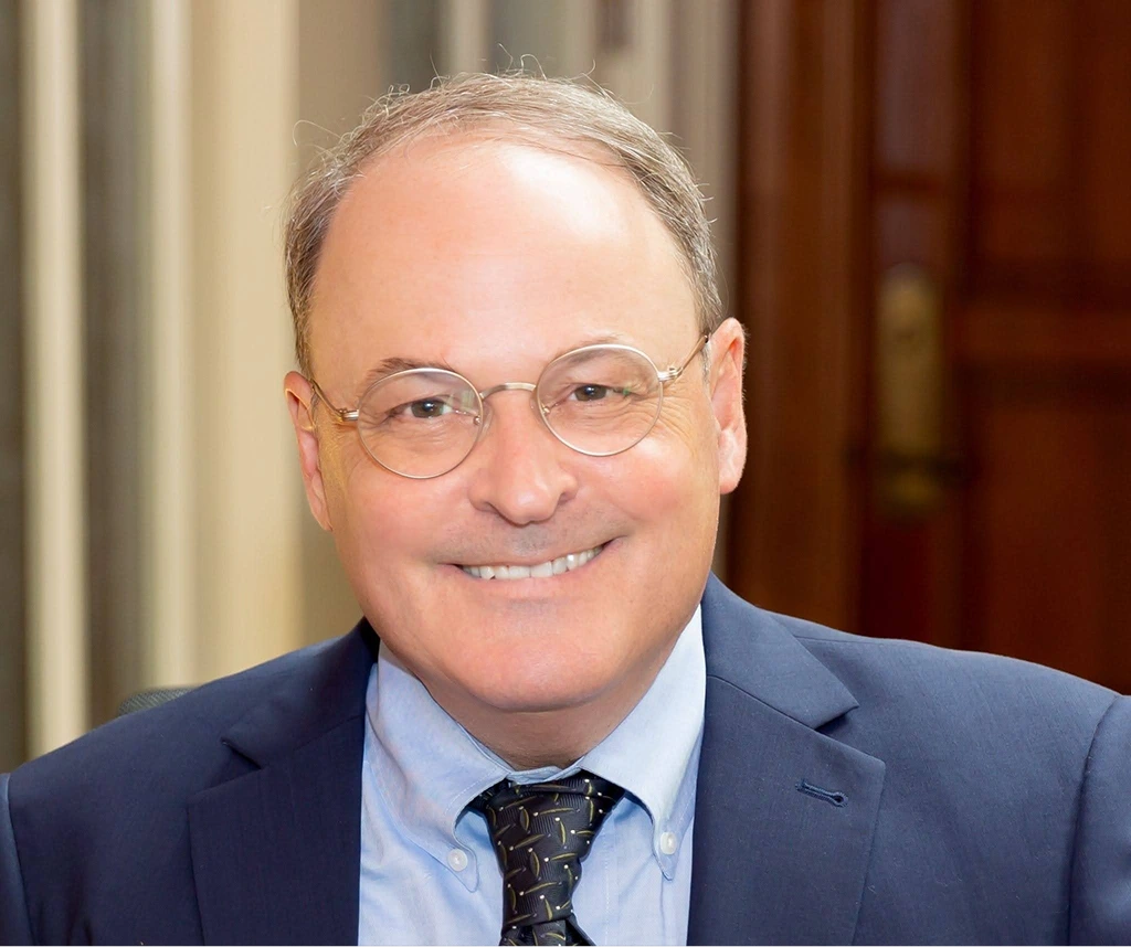 Portrait of a middle-aged man wearing glasses, a blue suit, and patterned tie, smiling.